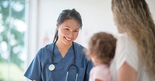 Nurse in scrubs smiling at child and mother