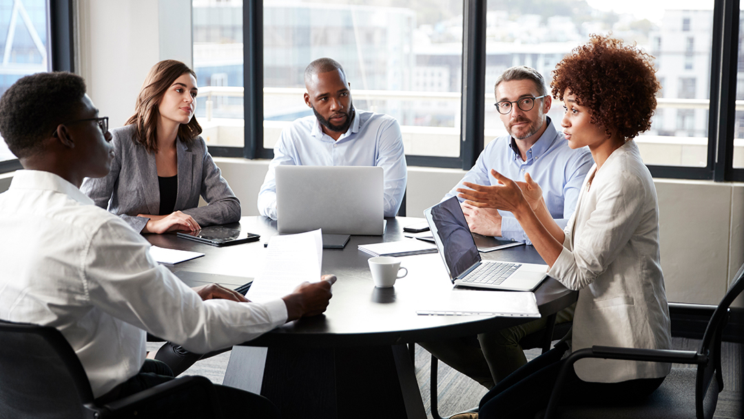 A team of business professionals listening to a woman speak in a meeting