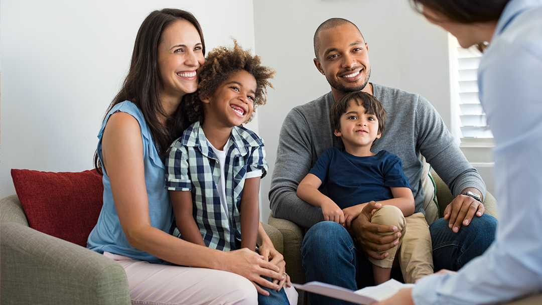 A family (two parents and two children) smiling as they meet with a health care professional